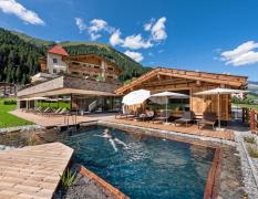 Alpinhotel berghaus spa Ansicht des Aussenpools mir Badehaus und dem Alpinhotel berghaus im Hintergrund